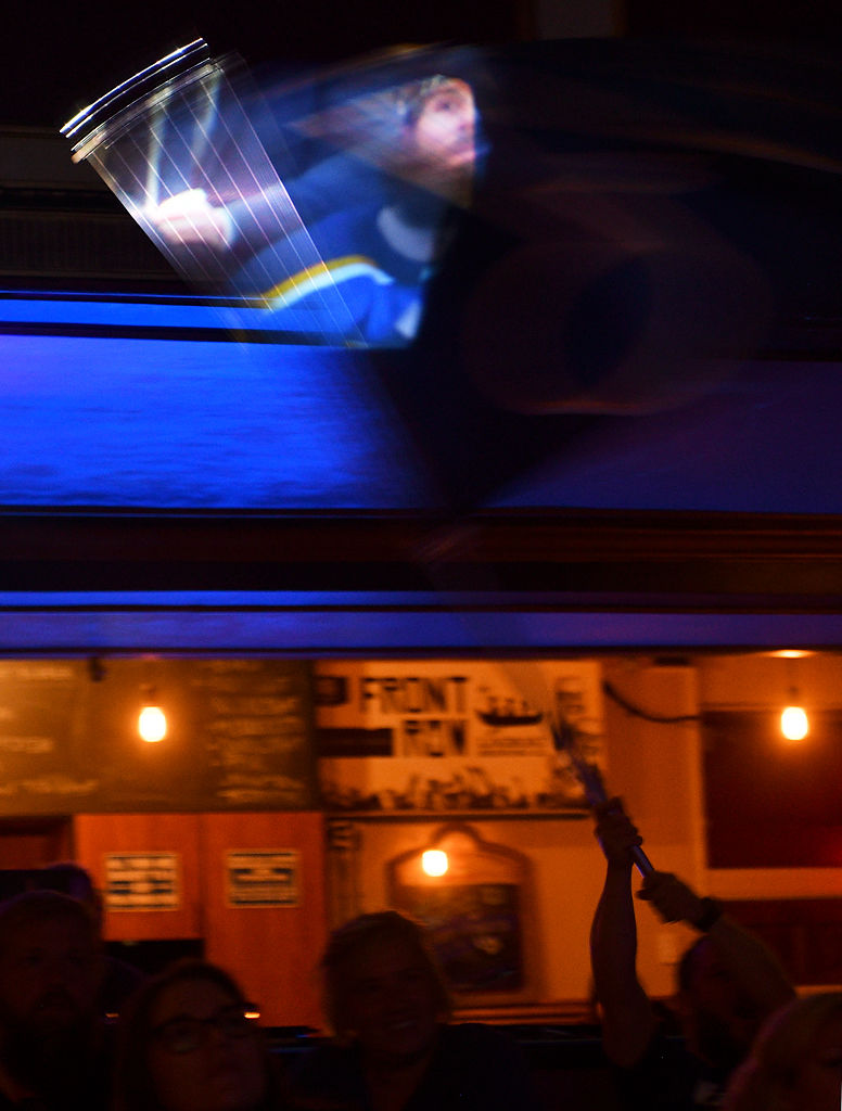The projection of the game passes through a waving Blues flag held by fan Mark Karr